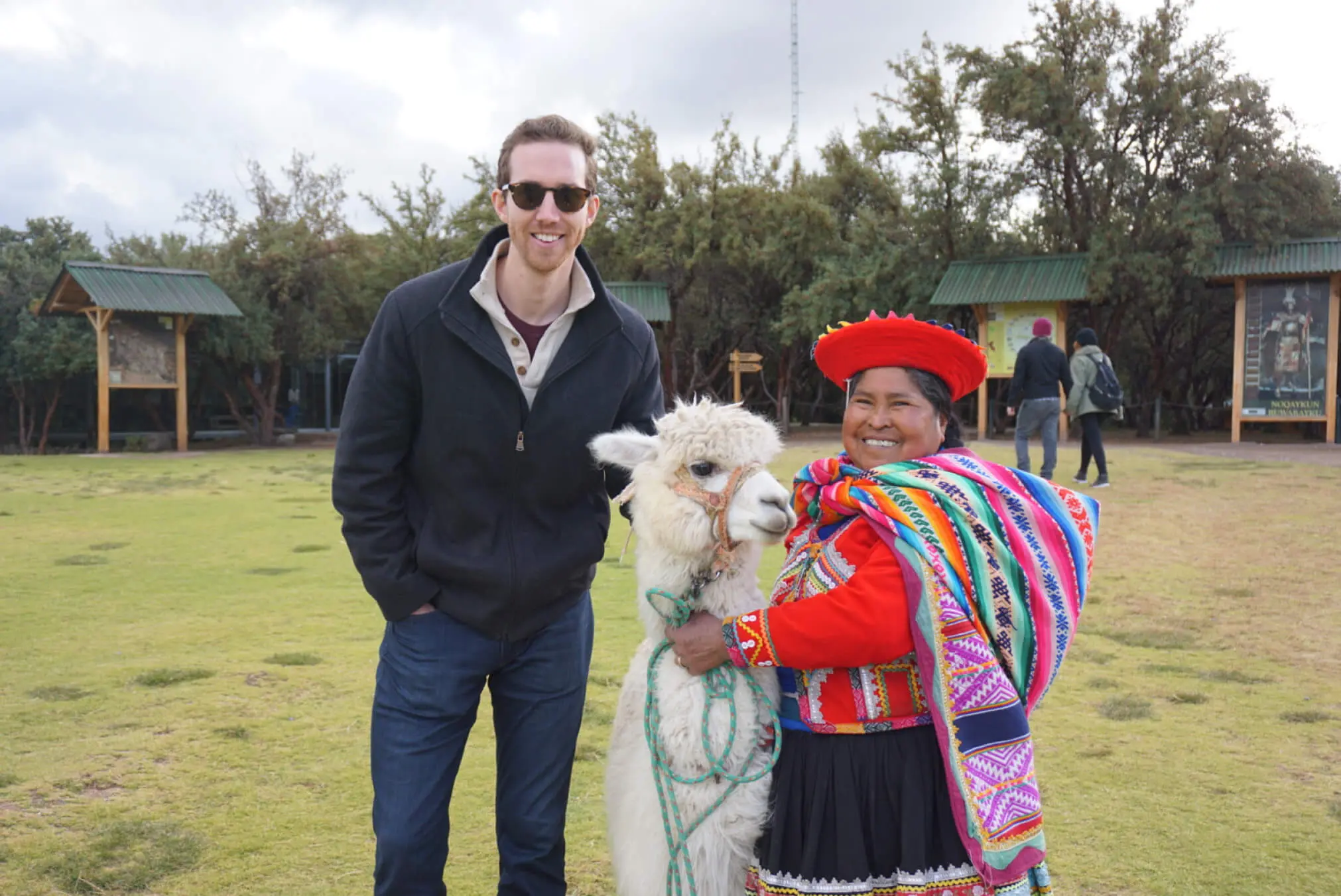 Fabric employee Spencer on a trip to Peru, smiling with a traditionally dressed woman and a llama.